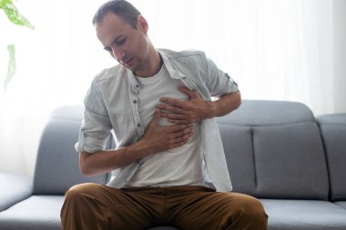 People, healthcare and health problem concept - unhappy young man having heart attack or heartache over gray background.