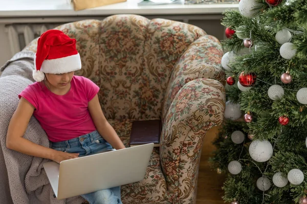 幸せな女の子は自宅でクリスマスツリーの下に贈り物を開き ビデオリンクを介してラップトップを介して祖父母と通信します クリスマスと新年のための休日の概念 — ストック写真