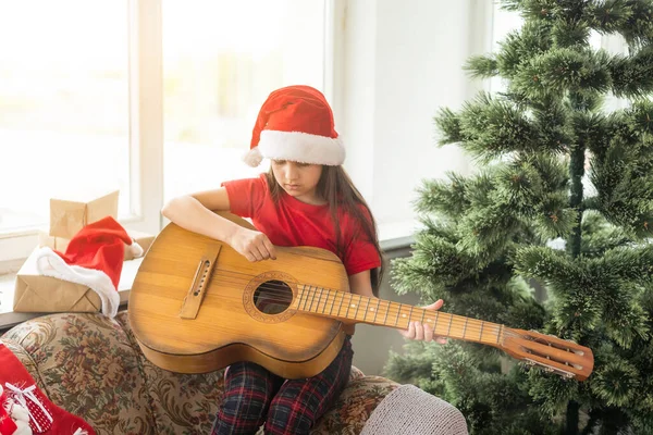 クリスマスツリーの背景で遊んで赤い帽子の幸せな女の子 居心地の良い装飾された家で冬の休暇を楽しんでいる才能のある子供 — ストック写真