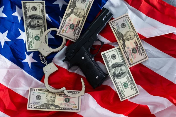 Gun, holster, handcuffs and cash in front of the American flag.