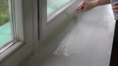 Bir kadın pencerenin yamaçlarını beyaz boyayla boyuyor, pencere açıklarını boya fırçasıyla boyuyor, pencere çerçevelerini beyaz boya ile boyuyor.