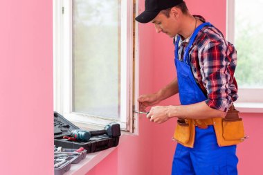 İnşaat işçisi plastik pencereyi tornavidayla tamir ediyor..