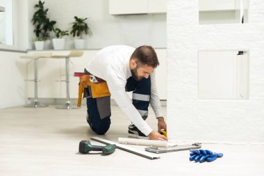 The craftsman measures the length of the plinth for cutting, installing the plinth on the corner of the wall, close-up installation.