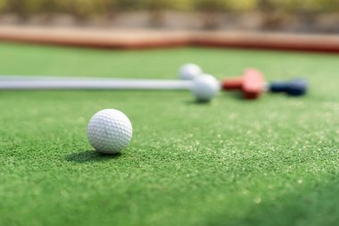 Assorted miniature golf putters and balls askew on synthetic grass