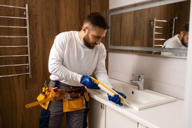 Profesyonel tesisatçı, üniformalı erkek işçi yeni daireye lavabo ve su borusu kuruyor..