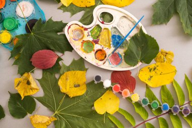 A child paints a picture of an autumn leaf with paints. Childrens hands. Favorite hobby, materials for creativity. High quality photo