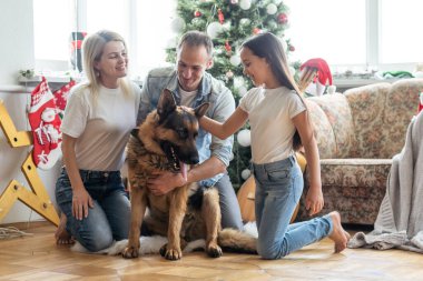 Dostu aile ile Noel ağacı yakınındaki köpek oynuyor. Onlar oturan ve gülüyor.