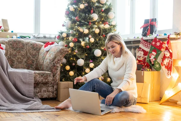 若い女性はクリスマスツリーの背景にラップトップでリモートで家庭で動作します 隔離休日は仕事だ 家で働いています — ストック写真