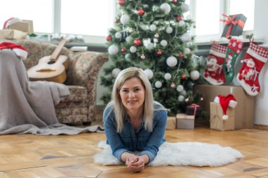 Noel zamanı gülümseyen bir kadının portresi. Bulanık süslemeli Noel ağacı ve arka planda parlayan bir çelenk.