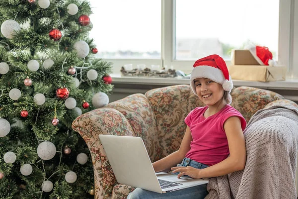 大きなリビングルームでクリスマスツリー クリスマスツリーの近くで女の子が遊んでいる ラップトップを持つ女の子は友人と通信します — ストック写真