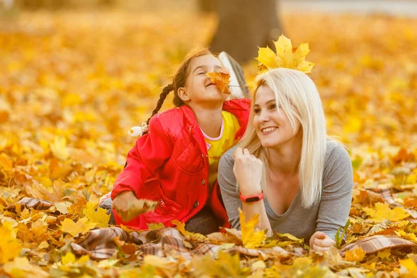 mother and daughter lying on the leaves at the autumn park