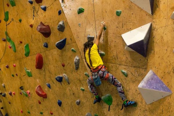 little girl climbing a rock wall indoor.