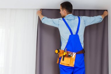 Genç yakışıklı bir adam ya da tamirci evdeki perdeleri takıyor, tadilat yapıyor.