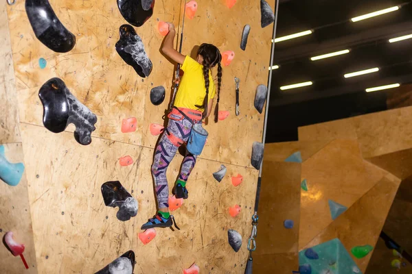 little girl climbing a rock wall indoor.