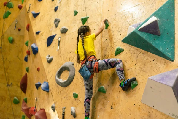 little girl climbing a rock wall indoor.