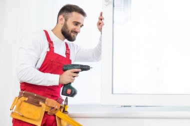 Yakışıklı genç adam yeni bir inşaat alanına pencere takıyor.