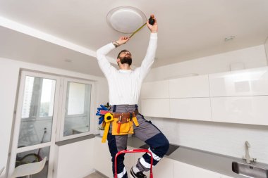Elektrik işçisi yeni dairede lamba monte ediyor.