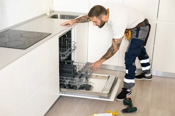 Technician or plumber repairing the dishwasher in a household.