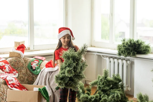Little Girl Makes Artificial Christmas Tree Wear Santa Hat Indoors — ストック写真
