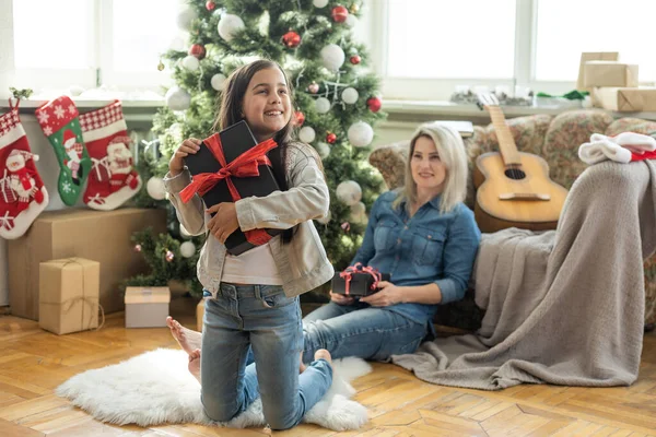 メリークリスマスとハッピーホリデー 陽気な母親とかわいい娘の女の子は贈り物を交換します 屋内で木の近くで遊んでいるお母さんと小さな子供 プレゼント付きの家族を愛する — ストック写真