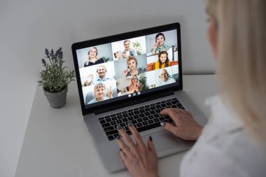 Beyaz kadın öğretmen okul çocuklarıyla video görüşmesinde bilgisayar ve dizüstü bilgisayar kullanıyor. Çevrimiçi eğitim karantina süresince evde tek başına kalıyor.
