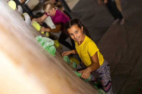 Instructors helping children climb wall in gym.