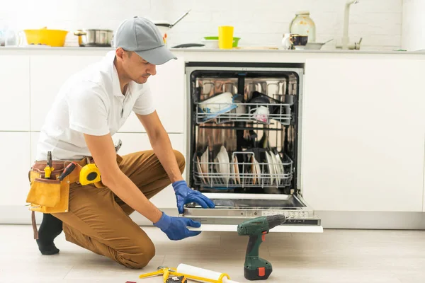 Üniformalı Tamirci Mutfaktaki Bulaşık Makinesini Tamir Ediyor Genç Adam Uzman — Stok fotoğraf