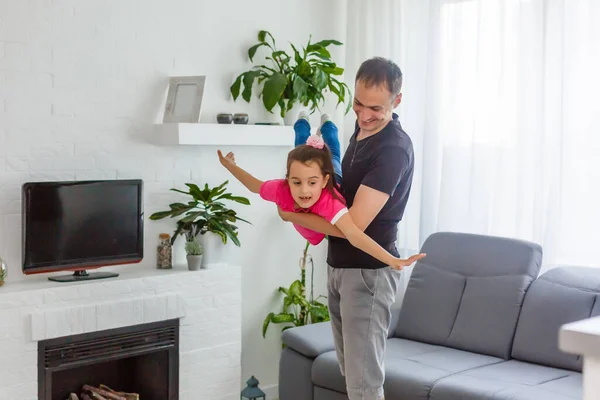 飛ぶことができる 幸せなお父さんは居間に立っている間に彼の小さな娘を持ち上げている — ストック写真