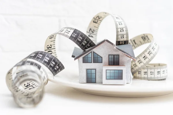 measuring tape and toy house in a white plate.