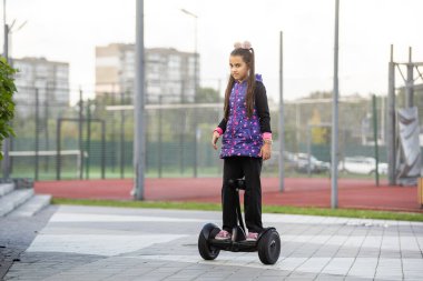 Elektrikli scooter kullanan küçük bir kız. Kişisel çevre taşımacılığı, jiroskoplu scooter, akıllı denge çarkı. Popüler elektrik taşımacılığı.