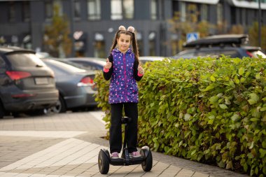Dışarıda elektrikli scooter 'ın üzerinde duran mutlu küçük kız..
