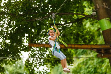 Yazın gökyüzü halat parkında miğferli ve koşumlu küçük bir kızın portresi.