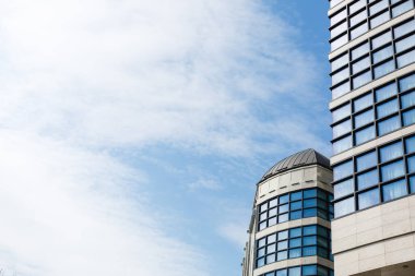 Büyük şehirde gökdelenler, arka planda mavi gökyüzü. Cam cepheli modern ticari binalar. Bulutlu gökyüzü pencere camına yansıyor. İnşaat, gayrimenkul, modern mimari
