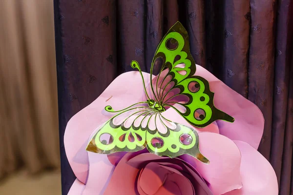 Home decor. Plastic colored butterfly on pink flower. Purple background