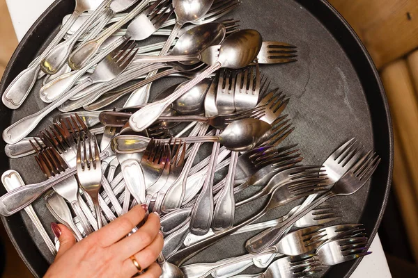 Stainless spoons, forks and knives on plate. Woman hand taking fork. Restaurant cutlery