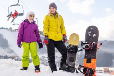 Snowboard yapan anne ve kızı karda oynuyorlar.