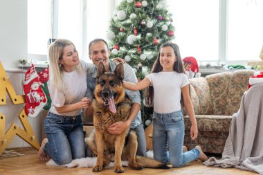 Gülümseyen aile ve kız ve köpek Noel ağacının yanında hediyelerle oturuyor..
