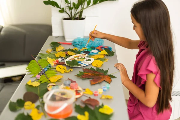 little girl paints leaves with brush at home, autumn art. High quality photo