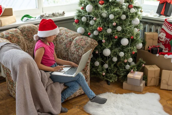 大きなリビングルームでクリスマスツリー クリスマスツリーの近くで女の子が遊んでいる ラップトップを持つ女の子は友人と通信します — ストック写真