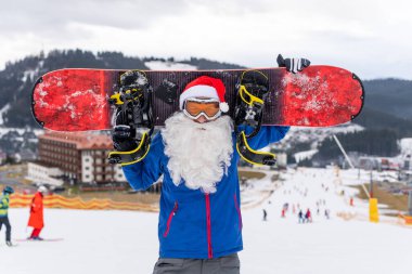 Kar kayağına karşı kar kayağı yapan Noel Baba. Kayak merkezi manzarası ve mavi gökyüzü. Yeni yıl veya xmas tebrik kartı.