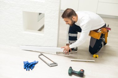 The craftsman measures the length of the plinth for cutting, installing the plinth on the corner of the wall, close-up installation.