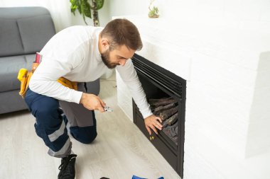 Professional technician with screwdriver installing electric fireplace in room.