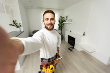 Yakışıklı, neşeli tamircinin portresi. Akıllı telefondan selfie çekiyor. Gömlek ve tulum giyiyor..