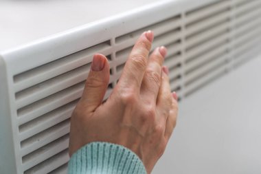 Kazaklı bir kadının yakın çekimi beyaz duvarın arkasındaki akünün üzerinde ellerini ısıtıyor. Makro kadın eli fotoğrafı, kopyalama alanı. Kışın gaz tasarrufu kavramı. Avrupa 'da gaz krizi.