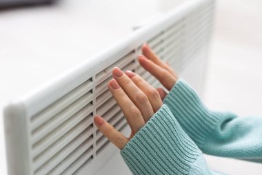 Kazaklı bir kadının yakın çekimi beyaz duvarın arkasındaki akünün üzerinde ellerini ısıtıyor. Makro kadın eli fotoğrafı, kopyalama alanı. Kışın gaz tasarrufu kavramı. Avrupa 'da gaz krizi.