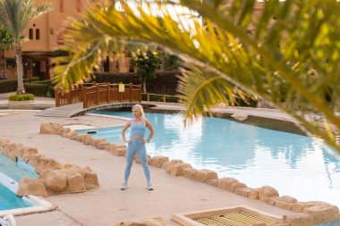 Gündoğumunda yoga meditasyonuyla günaydın. Sağlığını korumak için havuz başında pratik yapan aktif bir kadın. Yaz tatilinde kadın fitness eğitimi, spor aktiviteleri.