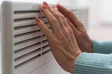 Bir kadın eli beyaz bir ısıtıcıya tutunuyor. Isıtma kavramı.