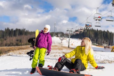 Anne ve kızı kış tatilinde snowboard yapıyor.