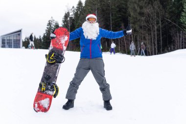 Noel Baba şapkalı bir adam kayak merkezinde snowboard yapıyor.