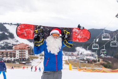 Kayak merkezinde kar kayağı yapan Noel Baba şapkalı bir adam.